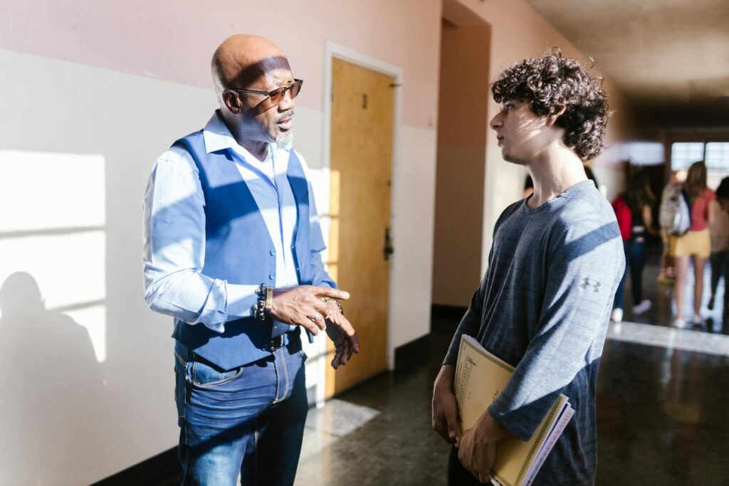 A teacher and student engaging in a discussion in a school hallway.