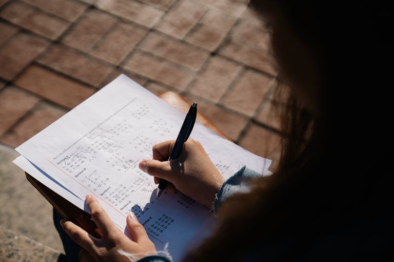A person writing calculations on a mathematical worksheet with a pen outdoors.